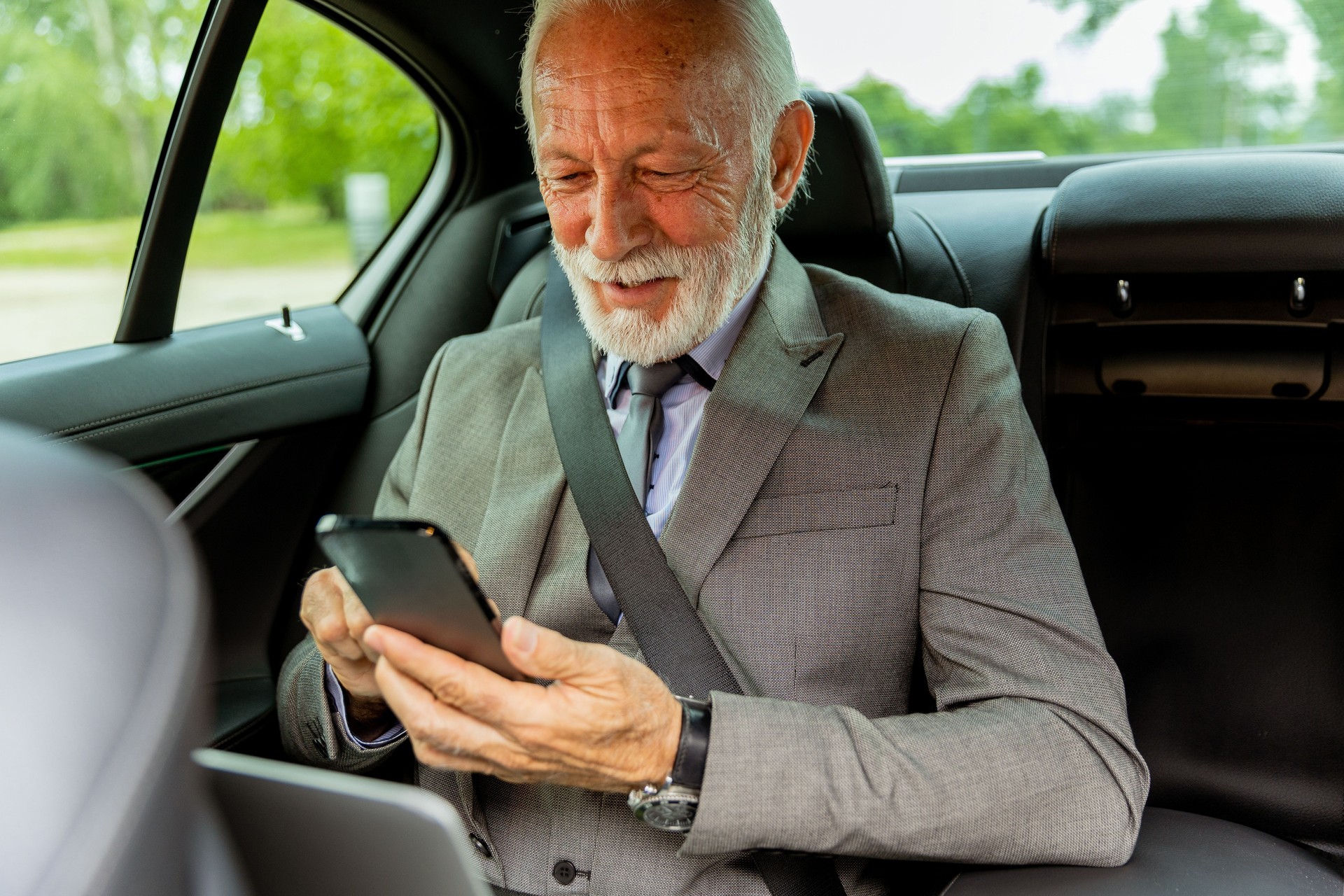 Elderly businessman checking his smartphone while traveling in a luxury sedan